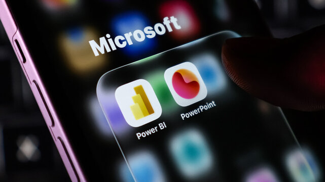 Closeup of a smartphone screen displaying microsoft app icons including power bi and powerpoint with a finger touching the display