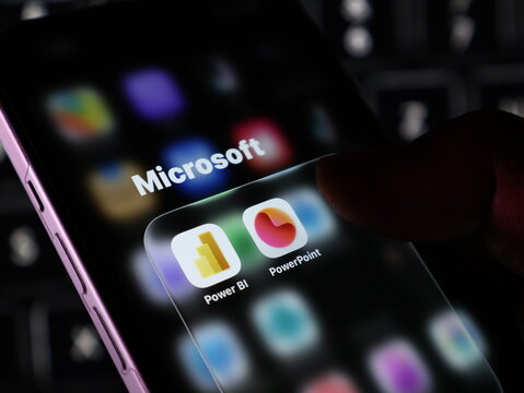 Closeup of a smartphone screen displaying microsoft app icons including power bi and powerpoint with a finger touching the screen