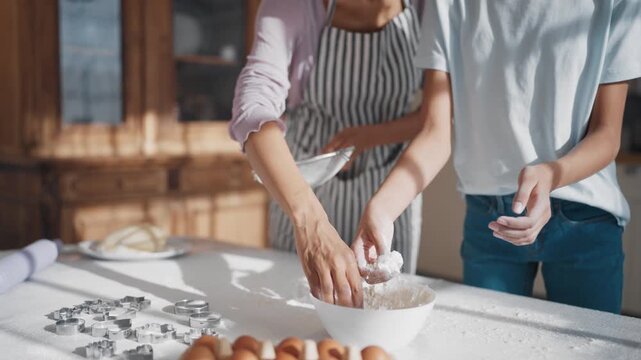 Woman teaching her teen daughter to cook, ladies baking tasty sweet cookies. Teenage girl learning to bake traditional family meal for dinner, sifting flour on tabletop, slow motion details shot