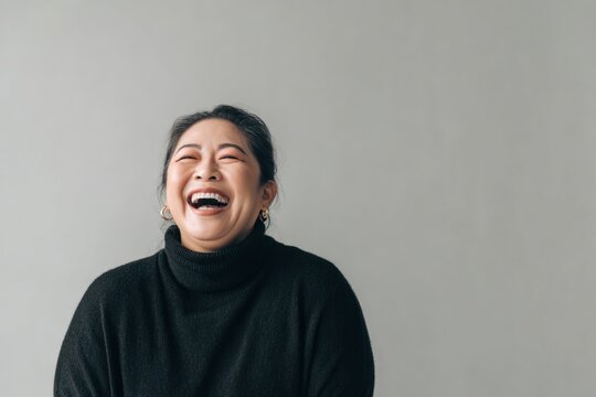 Laughing heartily, a joyful plus-size Asian female architect in her 40s with fair skin wears a black turtleneck sweater.