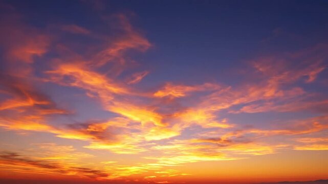Wide angle view of a vibrant sunset sky with a color gradient from deep blue to bright orange and yellow featuring scattered wispy clouds illuminated by the low sun at dusk.