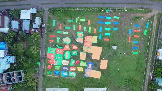 Aerial drone footage of multiple shapes tarpaulins, full of corn kernels on drying process, with local farmers working on them, in Tanju village, Manggelewa, Dompu regency, Sumbawa island, Indonesia