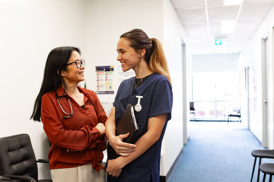 Two healthcare professionals happily conversing in clinic hallway
