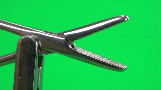 Close-up of a sterile metallic surgical grasper with open serrated jaws against a bright green background.