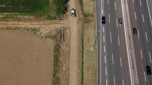 Juxtaposition of Old and New: An aerial view showcases a clear contrast between a dusty dirt road leading to a modern highway, separating agricultural fields from a transportation artery.