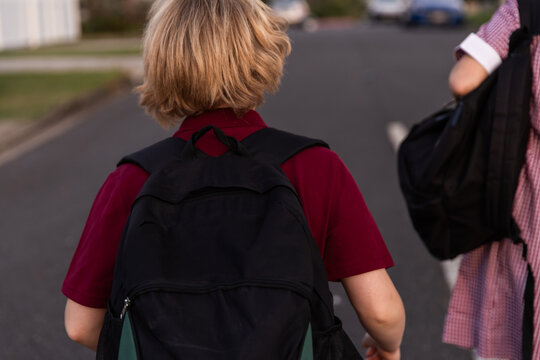 kids with black backpacks and wearing uniform walking on a street