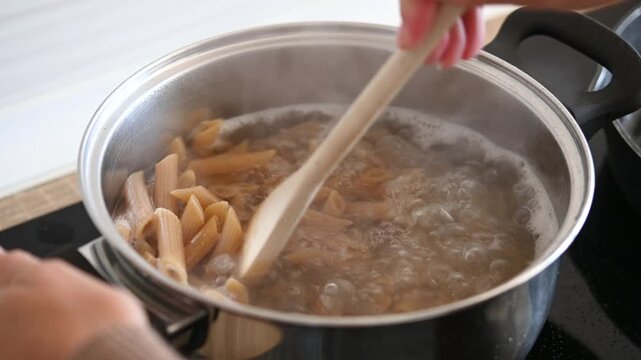 Woman stirring macaroni pasta in cooking pot