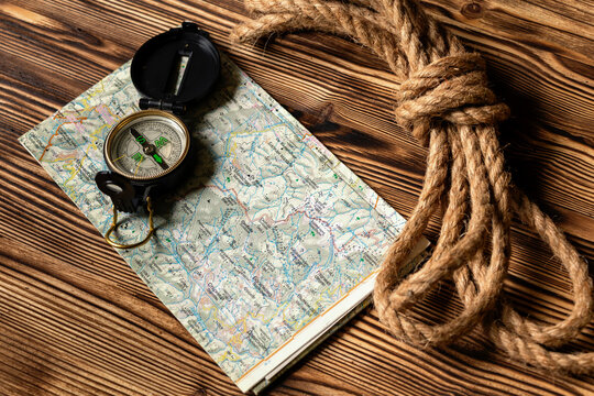 Vintage compass and rope on topographic map over wooden background