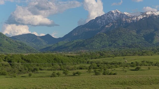 Majestic high tension power lines in a spring landscape with imposing snow capped Bucegi mountains, picturesque view, low altitude lateral aerial truck right