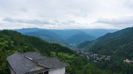 Obraz premium Scenic mountain view of Xijiang Miao Village, Guizhou, China with traditional roof and cloudy sky.