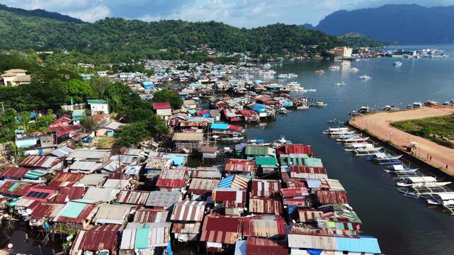 Aerial view of waterfront stilt houses in Coron Palawan Philippines with boats along narrow waterways dense coastal settlement and forested green hills