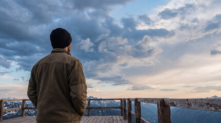 Man on a mountain viewpoint observing the majestic, cloudy sky and expansive snow-capped peaks below. © Dayne