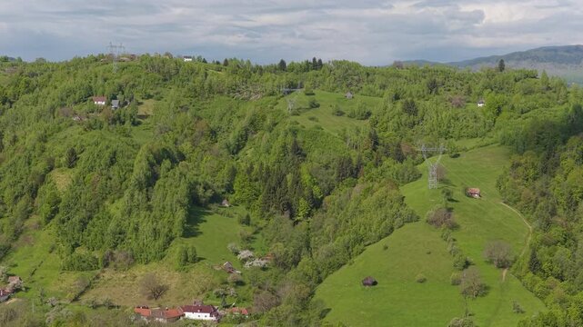 Detailed electricity pylons in a lush green mountain valley over Simon village on a sunny day, slow ascending drone flight, graded 4K