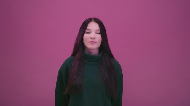 Portrait: teenage girl on pink background in green sweatshirt. Brunette woman face takes deep breath. Beautiful female, generation Z, alpha. Calm emotion and mindfulness, peaceful moment of relaxation
