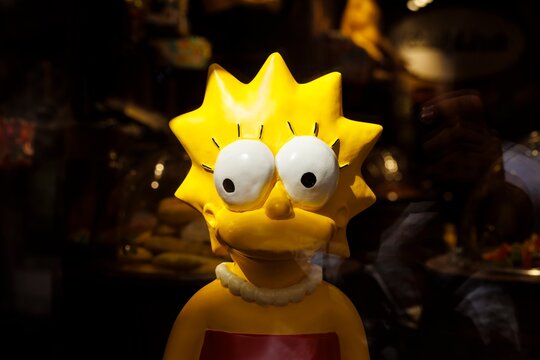 Lisa Simpson character figure illuminated in dark shop window with reflections and warm light