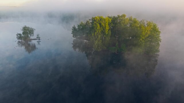 Aerial view of Venekotensee lake featuring small green islands enveloped in thick morning mist and fog with calm water reflections Niederkruchten, Nordrhein-Westfalen, Germany.