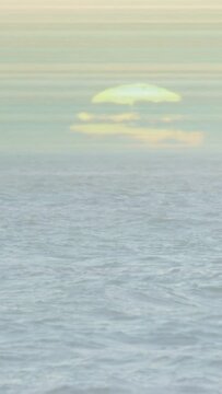 Vertical video: Camera panning upward to reveal low sun, ocean shifting and waves rolling to shore