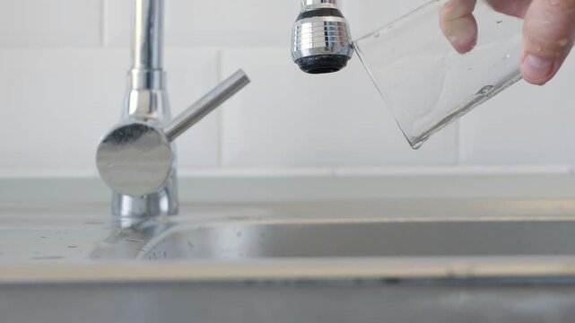 Man Throwing a Glass of Fresh Water in the Kitchen Sink.