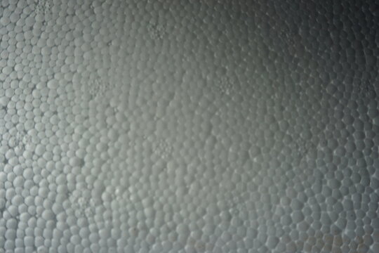 Macro shot of a white expanded polystyrene foam surface, showing the detailed cellular texture and structure. White plastic foam packaging material close-up.