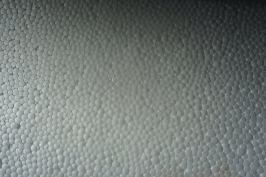 Macro shot of a white expanded polystyrene foam surface, showing the detailed cellular texture and structure. White plastic foam packaging material close-up.