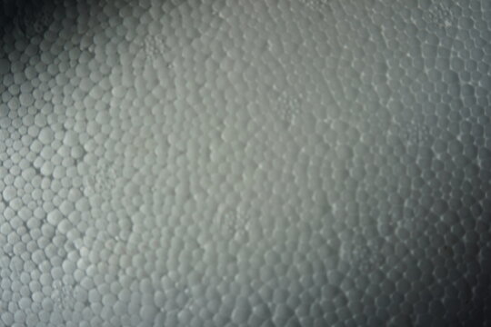 Macro shot of a white expanded polystyrene foam surface, showing the detailed cellular texture and structure. White plastic foam packaging material close-up.