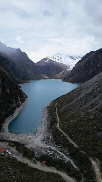 Huaraz, Peru: Aerial orbit vertical drone footage of stunning laguna paron in Caraz, Huaraz region, Peru, in Andes mountain with Piramide peak in cordillera blanca on a dramatic cloudy day.