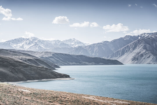 Landscape in the Pamir Mountains with a blue lake Yashilkul in the Tien Shan, a panoramic view of the highlands with snow-capped rocky peaks and the blue waters of the lake