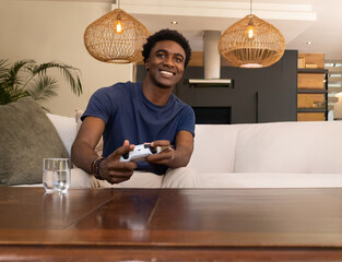 Fototapeta premium African American man sitting on sofa in modern living room holding white controller smiling