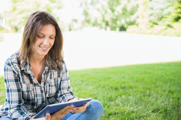 Teenage female sitting cross-legged on grass wearing plaid top and jeans holding tablet in case © wavebreak3