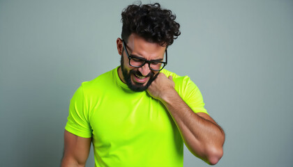 Fototapeta premium Man in neon shirt feels shoulder pain. He grimaces in discomfort from muscle ache after sport. Athlete needs recovery or therapy for injury.