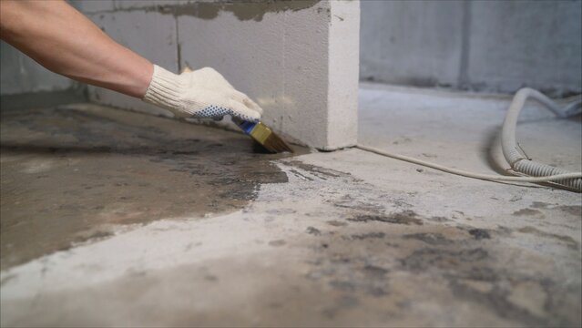 Worker in glove applying primer to concrete floor with brush