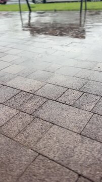 Wet urban pavement with puddles during rain near an empty outdoor area, rainy city scene, public walkway, urban texture, weather concept.