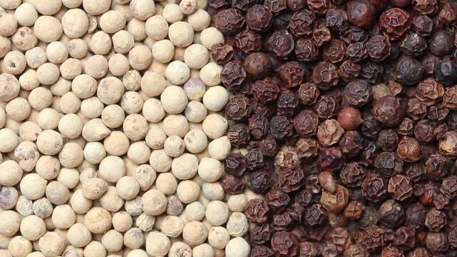 Top view of a slowly rotating pile of whole black and white peppercorns divided into halves.