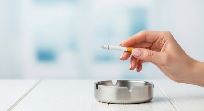 Close-up of a hand holding a lit cigarette over a metal ashtray, symbolizing smoking habit