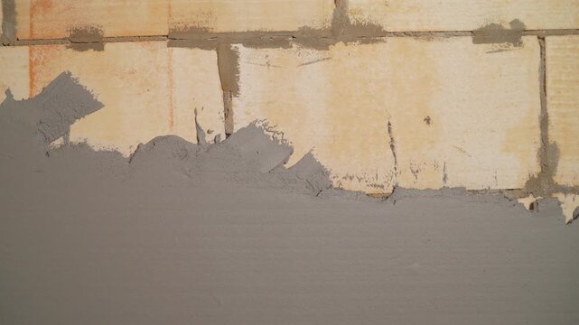 Close up of fresh grey cement plaster applied to yellow aerated concrete block wall. Rough texture meets smooth surface. Concept for construction, renovation, home improvement, and repair work
