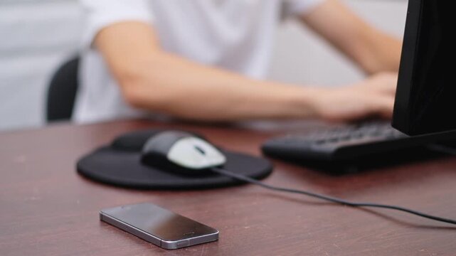 Man ignoring phone notification while working on computer at desk in office.