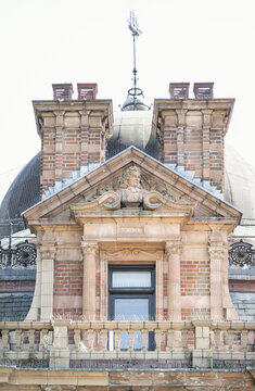 A meticulous brick and stone facade showcases ornate Edwardian architecture, centered around an elegant doorway framed by classic fluted columns. Above the entryway, a triangular pediment encloses a d