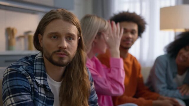 Sad pensive Caucasian man think alone home frustrated introvert feeling separated ignoring friends outsider male while African multiethnic women men laugh talk together friendship antisocial problem