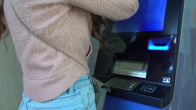Woman using automated teller machine to withdraw cash and check bank balance.