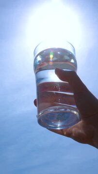 transparent glass glass of water with pure mineral water in hand against the sky with bright glare of the sun