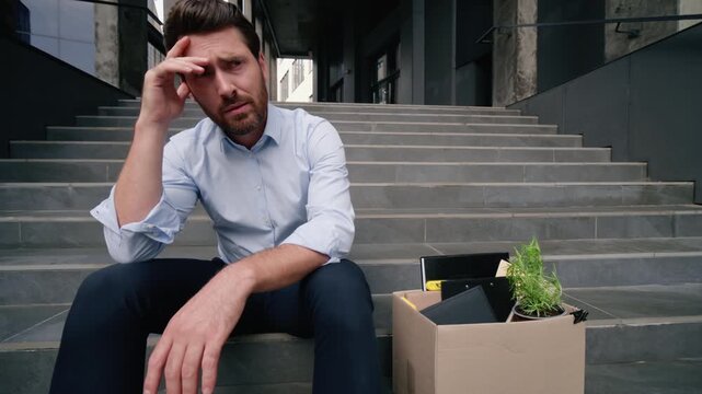 Pensive thoughtful Caucasian middle aged businessman sitting on stairs in city holding dismissal box fired guy unemployed male suffering burnout lost job sad frustrated dismissed business man outdoors