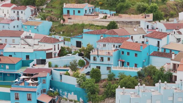 Aerial view of the famous blue-painted houses with terracotta roofs nestled in the green hills of Juzcar, Andalusia, Spain.