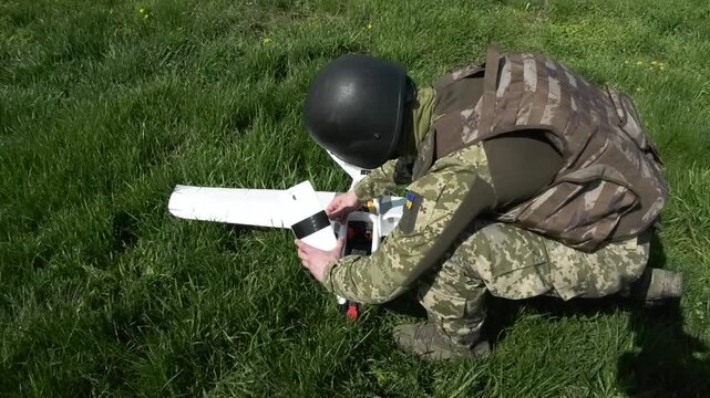 Serviceman preparing an aircraft-type drone for takeoff during a military mission. Concept of unmanned aerial systems, modern warfare technology, and deployment of strike drones in wartime conditions