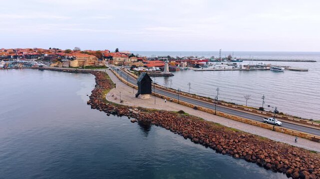 Aerial view of historic town causeway with black windmill and marina. A black wooden windmill stands on the causeway as the historic old town marina and red tiled roofs rise beyond.