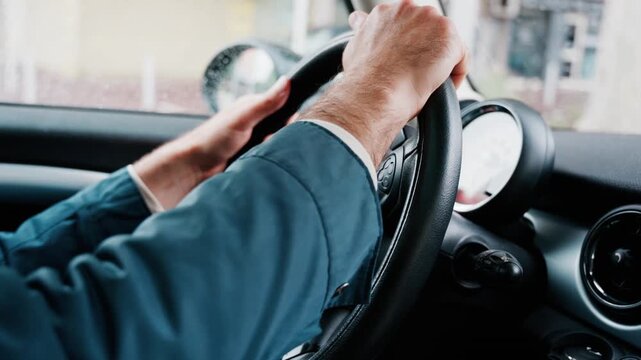 Close up of driver hands holding steering wheel during rainy day commute in city traffic.