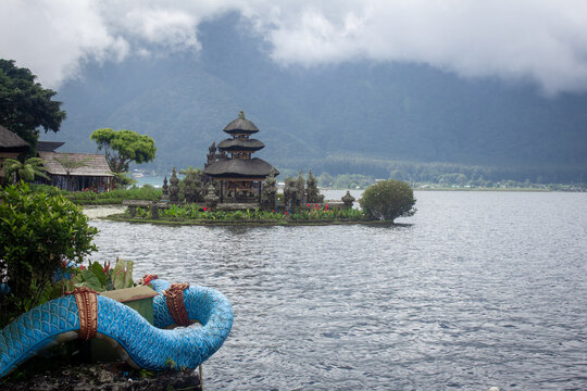 Ulun Danu Beratan Temple floating on Lake Beratan in Bali, Indonesia, with misty mountain backdrop and traditional dragon boat.