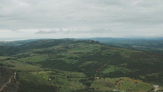 Aerial view of wind turbines on green rolling hills under an overcast sky in Casares, Andalusia, Spain.