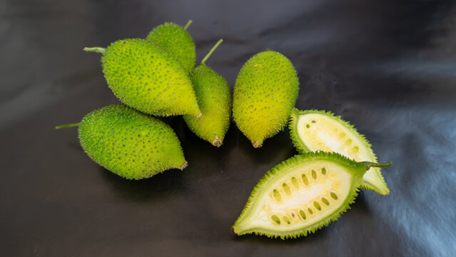 Fresh Spiny Gourd or Teasel Gourd on Dark Background with Cut Open Fruit Showing Seeds, Tropical Organic Vegetable and Healthy Asian Ingredient Close Up