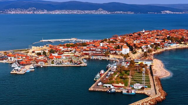 Aerial view of historic old town on a Black Sea peninsula with marina. Dense red tiled rooftops cover a historic peninsula as boats are moored along stone embankments flanked by open sea.