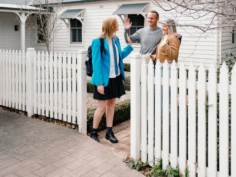 Parents waving goodbye to teenage daughter leaving for school on sunny day